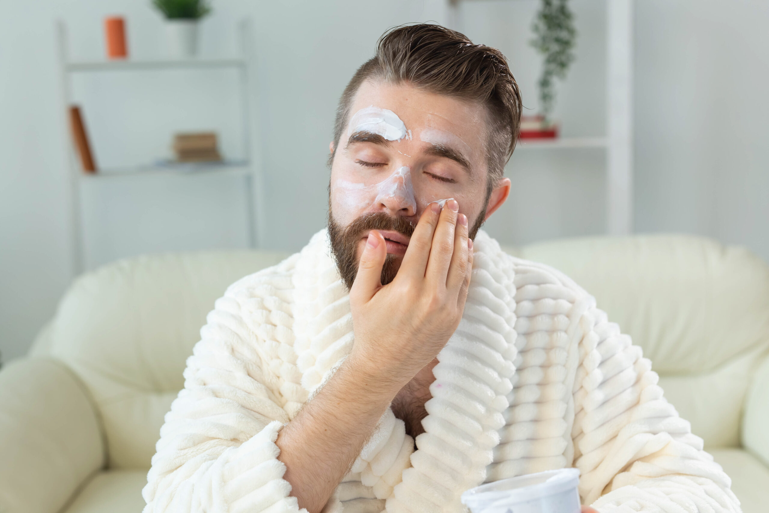 Closeup of handsome young man applying facial cream in front of mirror. Peptides for mens skin care